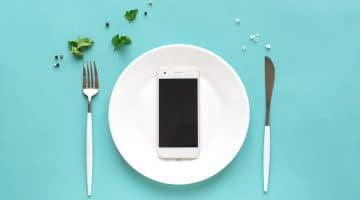 phone on a dinner plate with fork and knife on either side on teal background