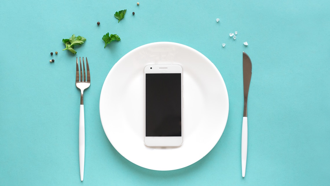 phone on a dinner plate with fork and knife on either side on teal background