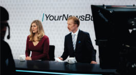 Two people sitting at an news anchor desk
